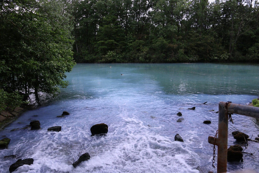 Wasser sprudelt in ein türkis aussehendes Gewässer zwischen Bäumen. 